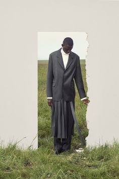 a man wearing a suit and tie standing in front of a white wall with grass