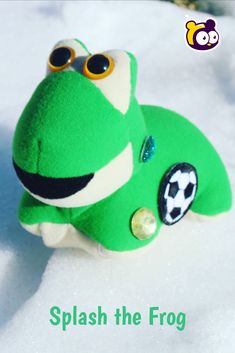 a green stuffed animal with big eyes sitting in the snow, says splash the frog