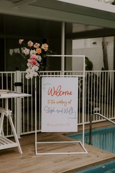 a welcome sign sitting on top of a wooden deck next to a swimming pool with flowers