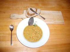 a white plate topped with soup next to a slice of bread on top of a wooden table