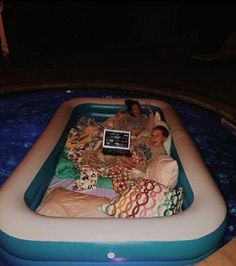 two people laying in an inflatable pool with a laptop