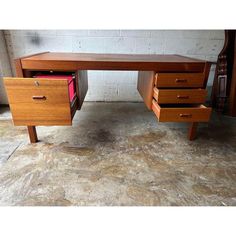 a wooden desk with two drawers and a file cabinet on the bottom drawer, in front of a white brick wall