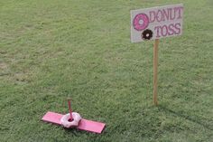 a donut toss sign sitting on top of a lush green field next to a pink plane