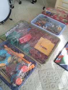 three plastic trays filled with toys on top of a floor next to a drum