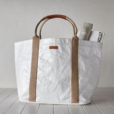 Market tote, gym bag, everyday carryall—this dynamo goes by all of the above. It’s fashioned from Uashmama’s signature washable paper and topped off with a water-resistant, glossy finish. (That means it’ll wipe down in a flash.) Shoutout to the inner pocket, magnetic closure, and cotton handles that give it extra versatility. AGGO® washable paper exterior. Cotton interior. Handles made of 85% recycled t-shirts. Water-resistant glossy finish. Generously sized, yet lightweight. Magnetic snap closu White Practical Travel Bag For Daily Use, Functional White Duffle Bag For Everyday Use, White Tote Duffle Bag For Everyday Use, Practical White Bags For Everyday Use, Everyday White Bag With Rolled Handles, White Everyday Tote Duffle Bag, Practical Everyday White Bags, Casual White Weekender Bag With Leather Handles, White Tote Weekender Bag With Top Carry Handle