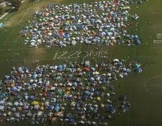 an aerial view of people holding umbrellas in the shape of letters on a soccer field