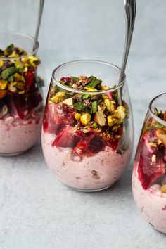 three glasses filled with food on top of a white table next to silver spoons