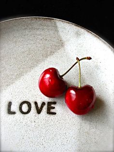 two cherries sitting on top of a plate with the word love written on it