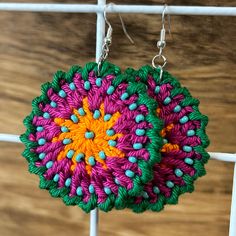 a pair of colorful earrings hanging from a white hook on a wooden surface with beads