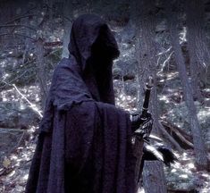 a person in a hooded cloak and hood holding a knife standing next to a tree