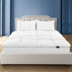 a bed with white sheets and pillows in a blue walled room next to a wooden floor