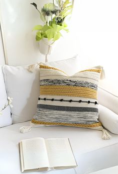 a white couch with an open book on it and a plant in the corner next to it