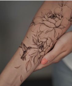 a woman's arm with flowers on it and a bird flying over the wrist