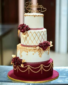 a three tiered wedding cake with red flowers and gold lettering on the top layer