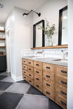 a bathroom with two sinks and mirrors on the wall next to a black tile floor