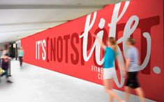 people are walking past a red wall with the words it's not easy