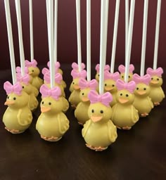 there are many little yellow ducks with pink bows on their heads and white sticks sticking out of them