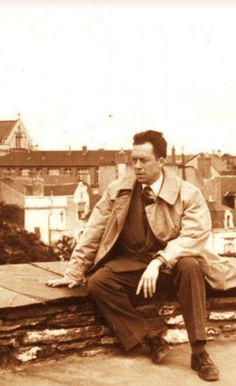 an old photo of a man sitting on a wooden bench in front of some buildings