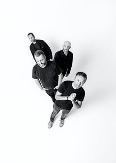 four men are standing in the middle of a white background, looking up at the camera