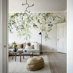 a living room with white furniture and green leaves on the wall