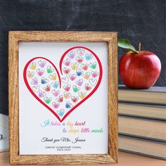 an apple and some books on a table next to a frame with a heart drawn on it