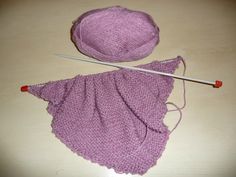 there is a purple knitted skirt and a ball of yarn next to the knitting needles