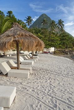 lounge chairs and umbrellas on the beach with mountains in the background