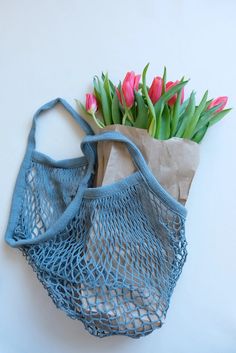 a blue net bag with pink tulips in it sitting next to a brown paper bag