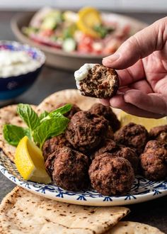 a hand holding a piece of meatballs over pita bread with lemon wedges