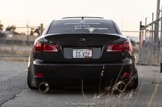 the back end of a black car parked in front of a fence