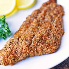 a piece of meat on a plate with lemons and parsley next to it