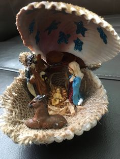 a small nativity scene in a shell on a table with other figurines