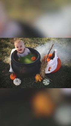 a baby sitting in a black pot filled with water and pumpkins on the ground