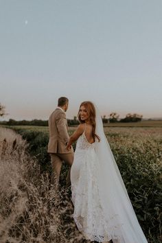 a bride and groom walking through tall grass