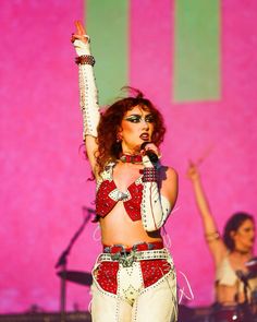 a woman in white and red outfit on stage with her hands up to the air