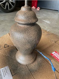 a large gray vase sitting on top of a cardboard box next to a blue cord