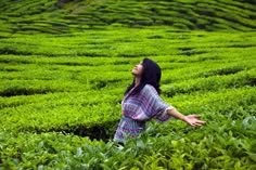 a woman standing in the middle of a green field with her arms out and looking up