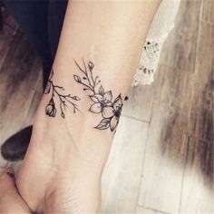 a woman's wrist tattoo with flowers and leaves on her left hand, in black ink