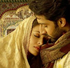 a man and woman cuddle in front of a birdcage with their eyes closed