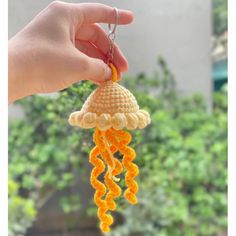 a hand holding an orange crochet jelly keychain hanging from a chain