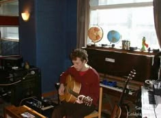 a young man sitting in a chair playing an acoustic guitar