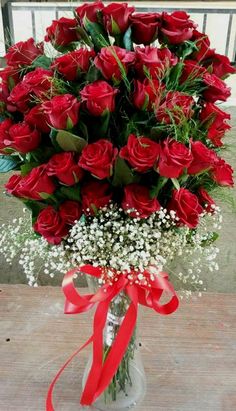 a vase filled with lots of red roses and baby's breath on top of a table