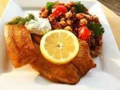 a white plate topped with fish, rice and lemon wedges next to a salad