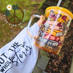 a person holding up a yellow coffee cup with books on it and butterflies painted on the side