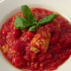 a white bowl filled with red sauce and garnished with green leafy leaves