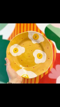 a person holding a yellow plate with eggs on it and smiling faces painted on the side