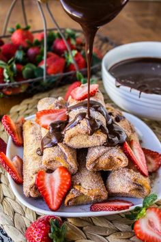 chocolate sauce being poured over strawberry crepes on a white plate with strawberries