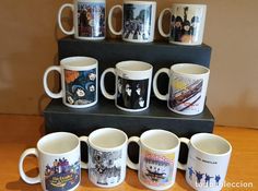 coffee mugs are lined up on a shelf in front of a wall with pictures