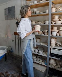 a woman standing in front of shelves filled with pottery