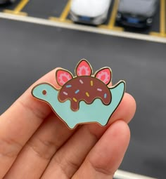 a hand holding a donut pin with sprinkles and chocolate frosting